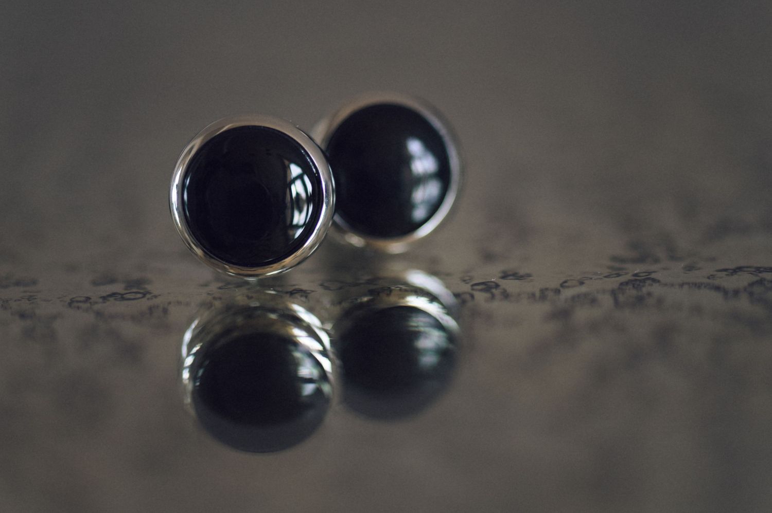 Elegant black onyx silver cufflinks reflected on a dark textured surface, perfect for formal occasions.