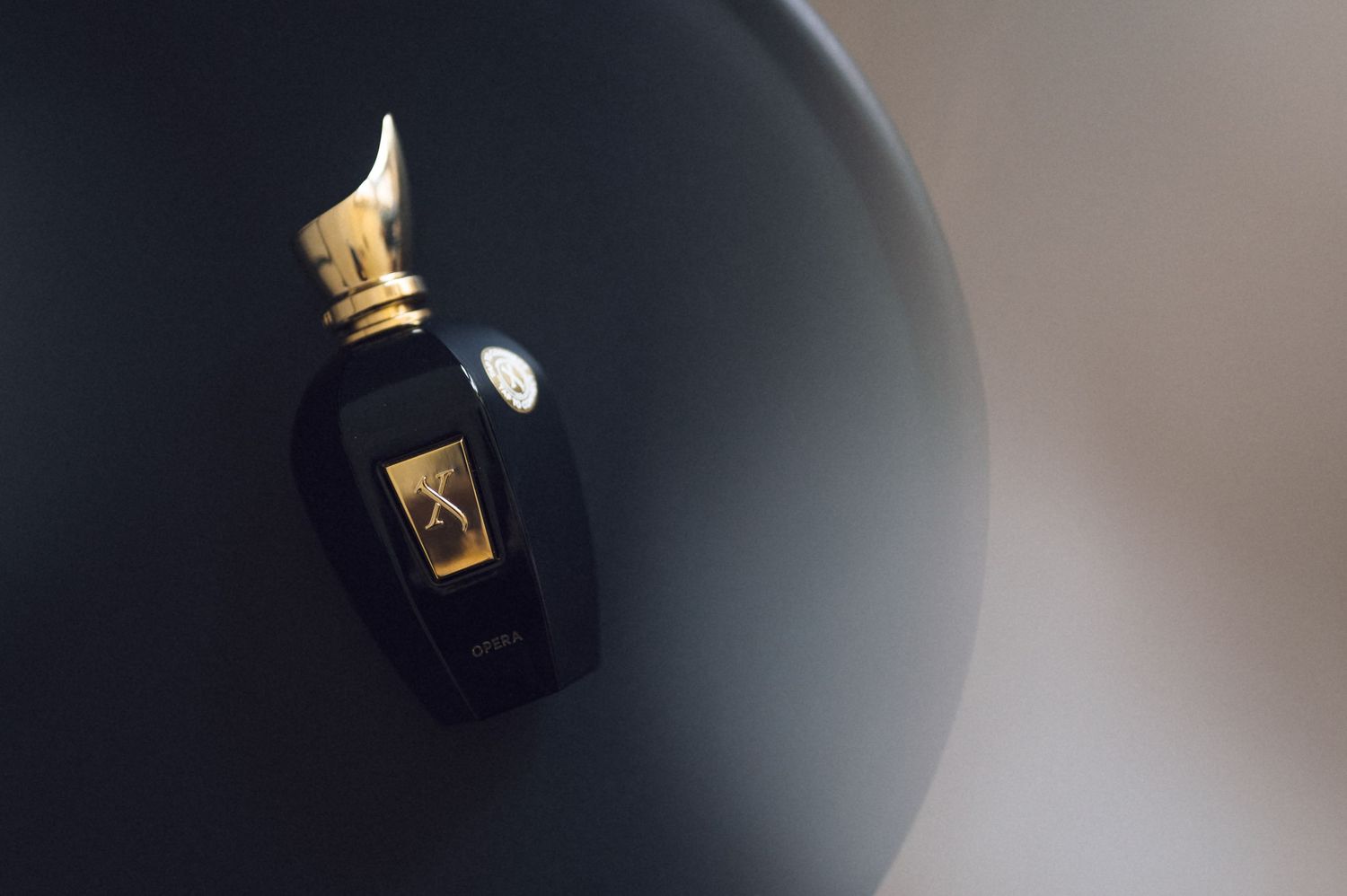 Luxury black and gold perfume bottle resting on a dark sphere, elegant fragrance presentation.