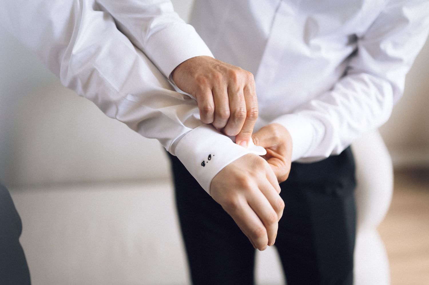 Man in white dress shirt fastening cufflinks on his wrist, preparing for a formal event or wedding.