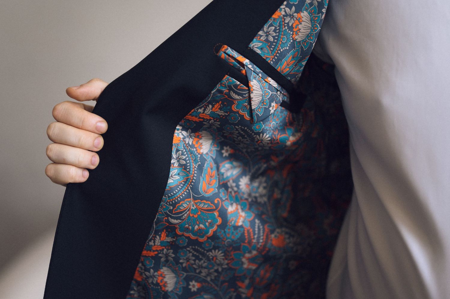 Man opening dark navy suit jacket to reveal vibrant paisley patterned lining in teal, orange, and blue.