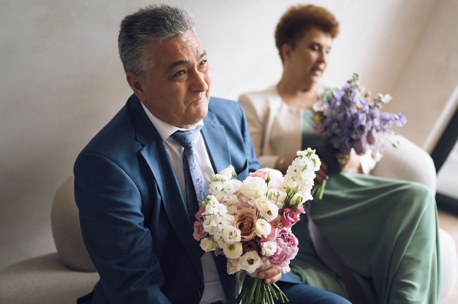 Middle-aged man in blue suit holding a bouquet of pink and white flowers at a wedding ceremony.