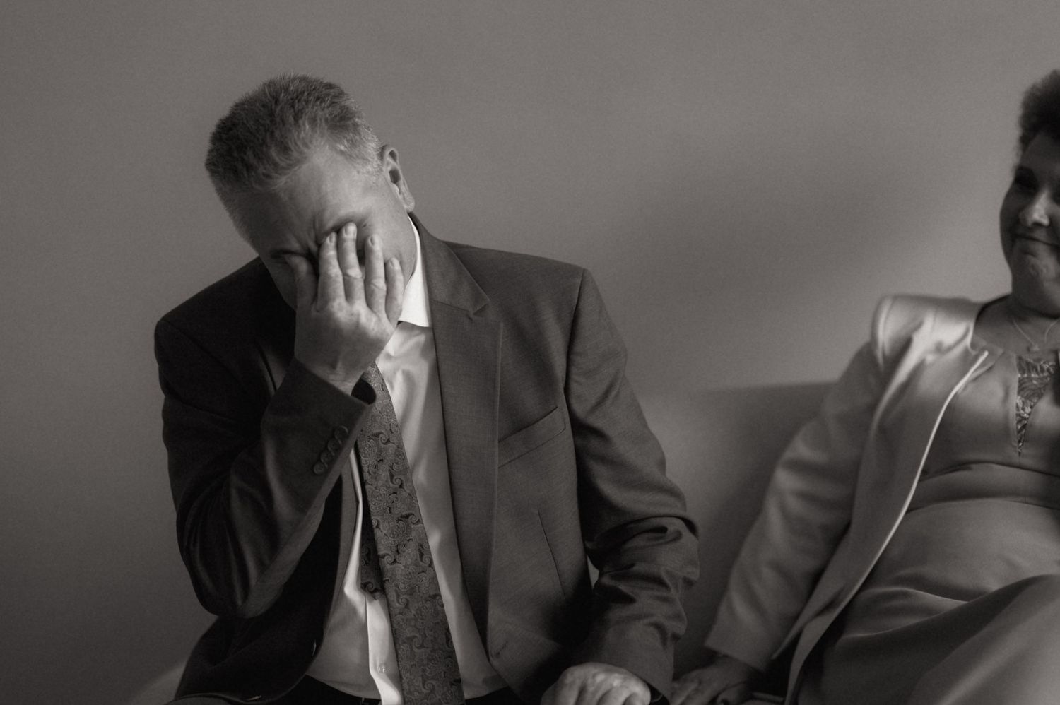 Black and white photo of two elderly people sitting, man covering face with hand in distress.