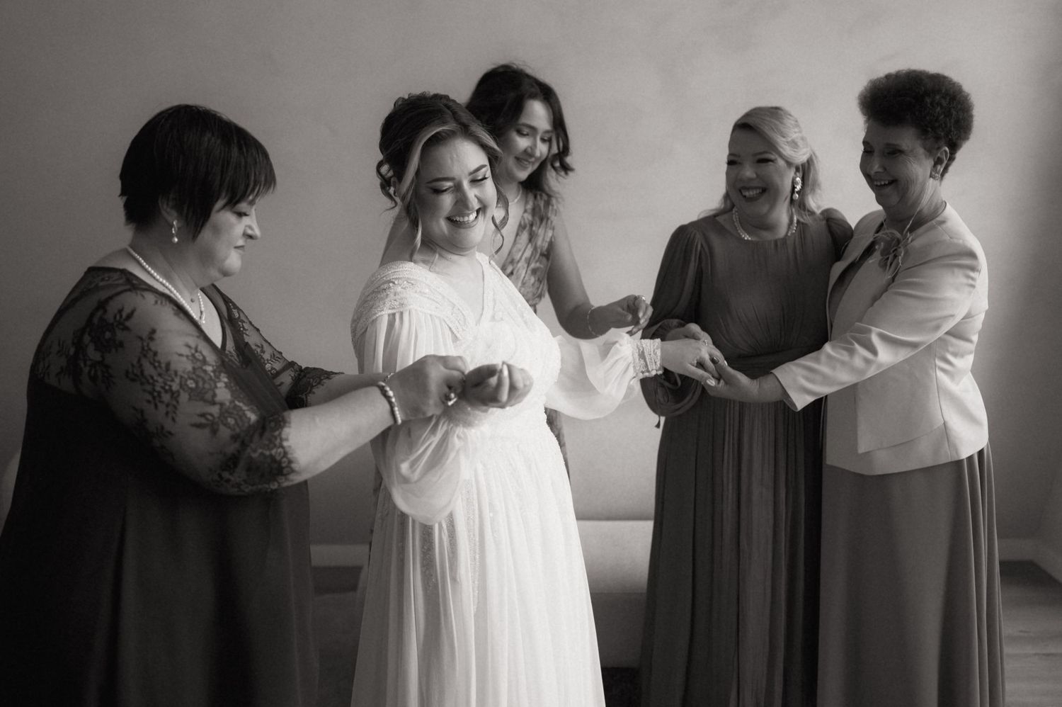 Bride in white gown gets ready with bridesmaids and family in black and white wedding photo.