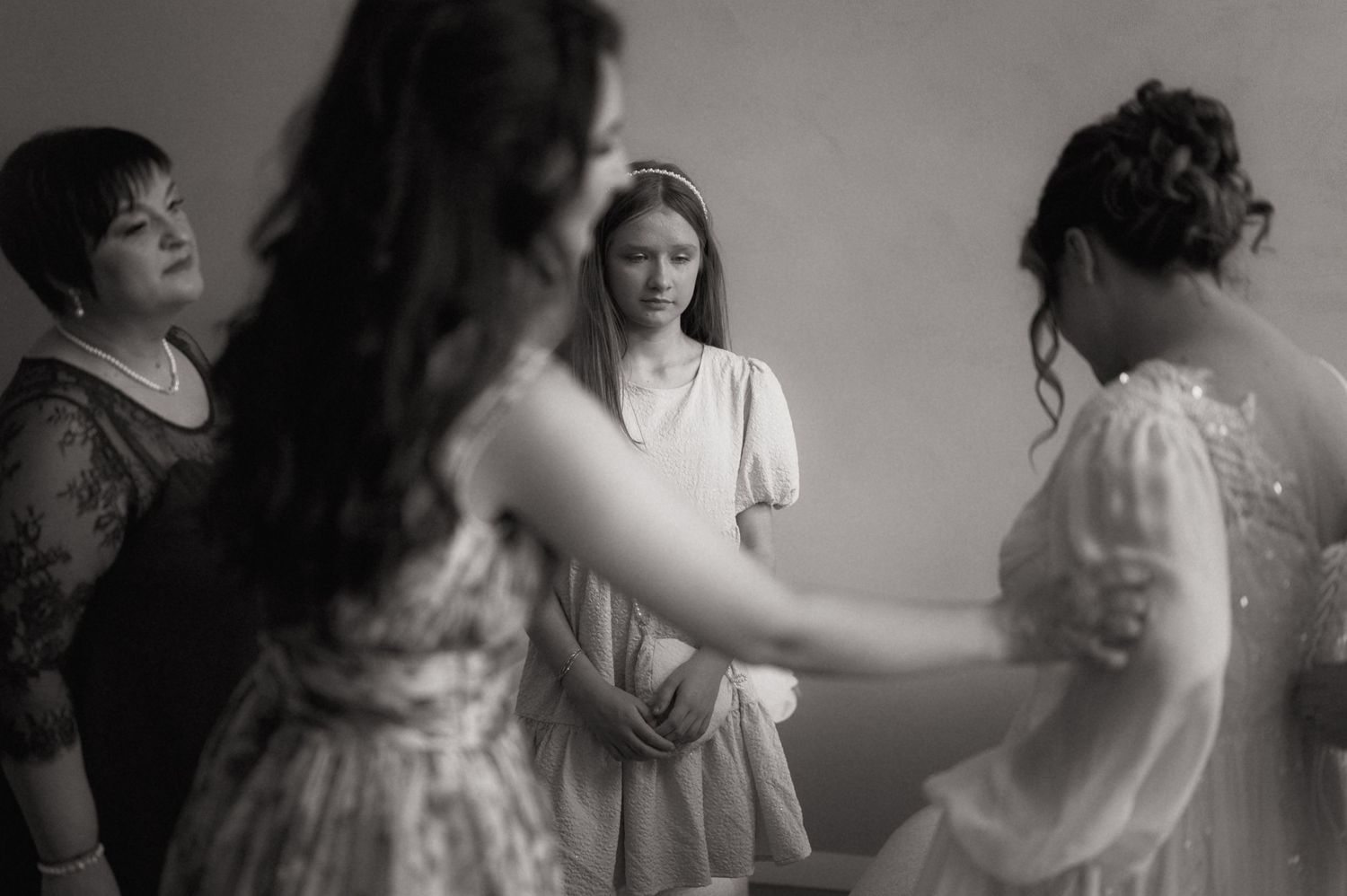 Black and white photo of a bride in white dress surrounded by bridesmaids helping her prepare for her wedding day.