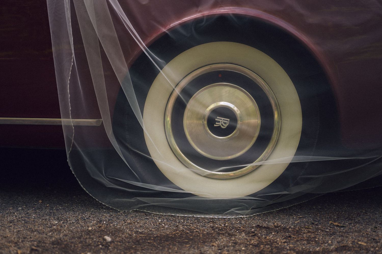 Vintage car wheel with white wall tire and chrome hubcap covered in clear plastic wrap on dark pavement.
