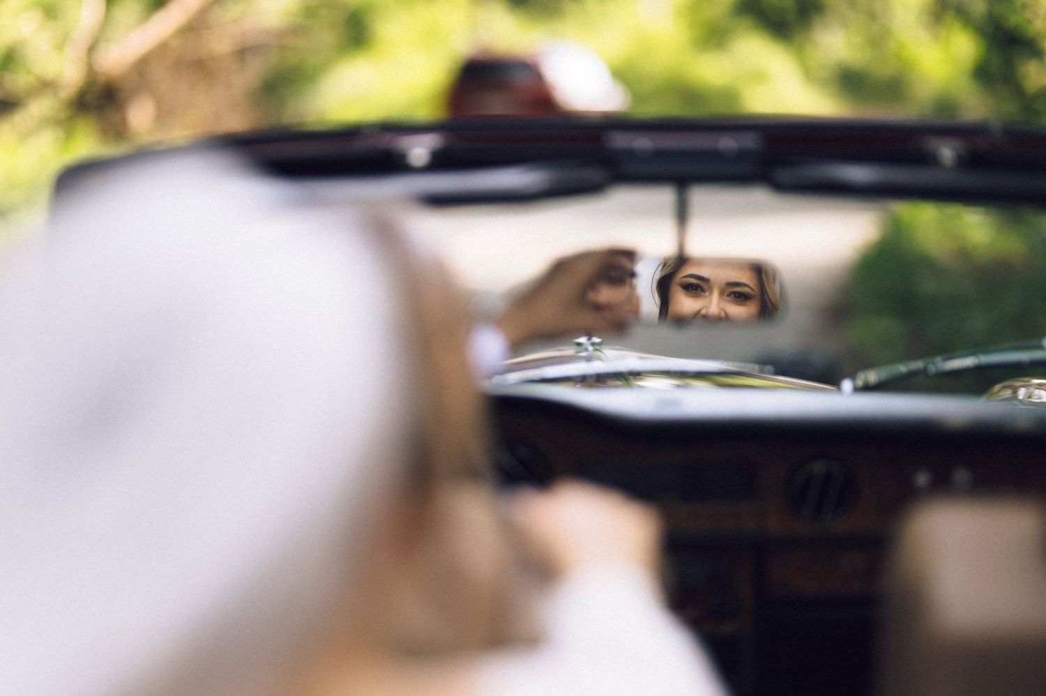 Bride smiling reflected in a vintage car mirror on her wedding day.
