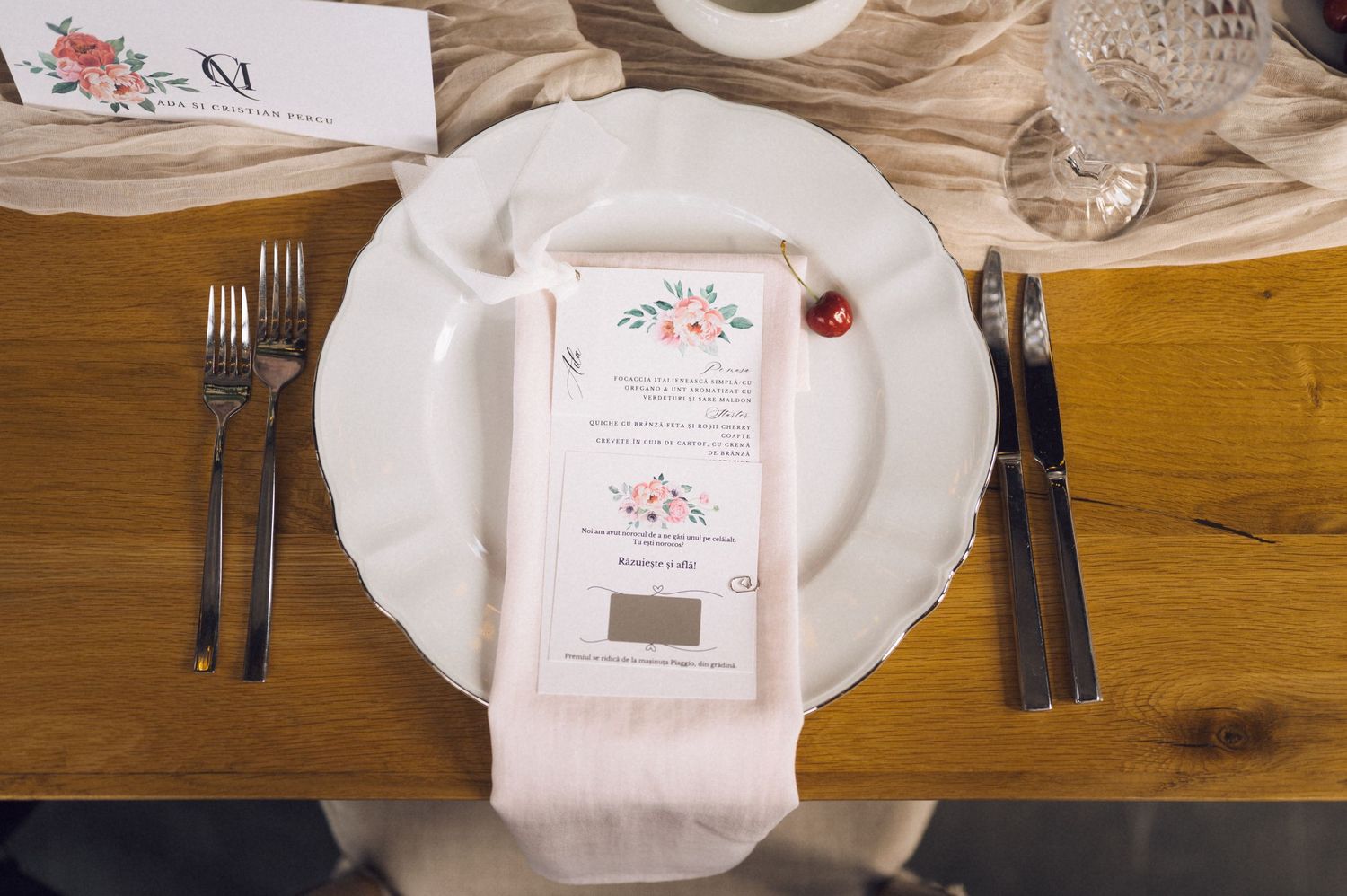 Elegant wedding place setting with floral menu card on white plate, flanked by silverware on rustic wood table.