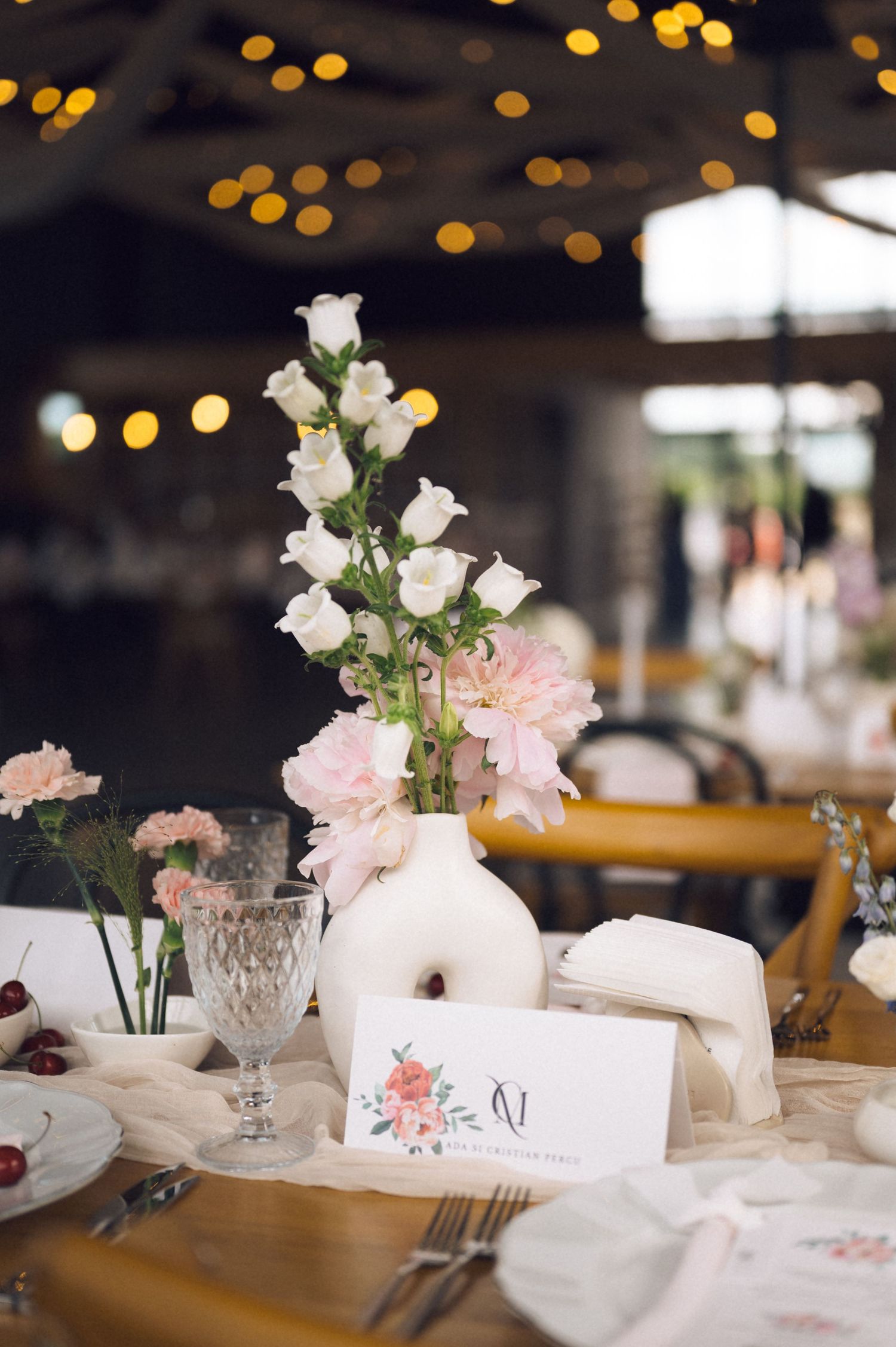Elegant wedding table centerpiece with white and pink flowers in a white vase, crystal glassware, and floral place cards.