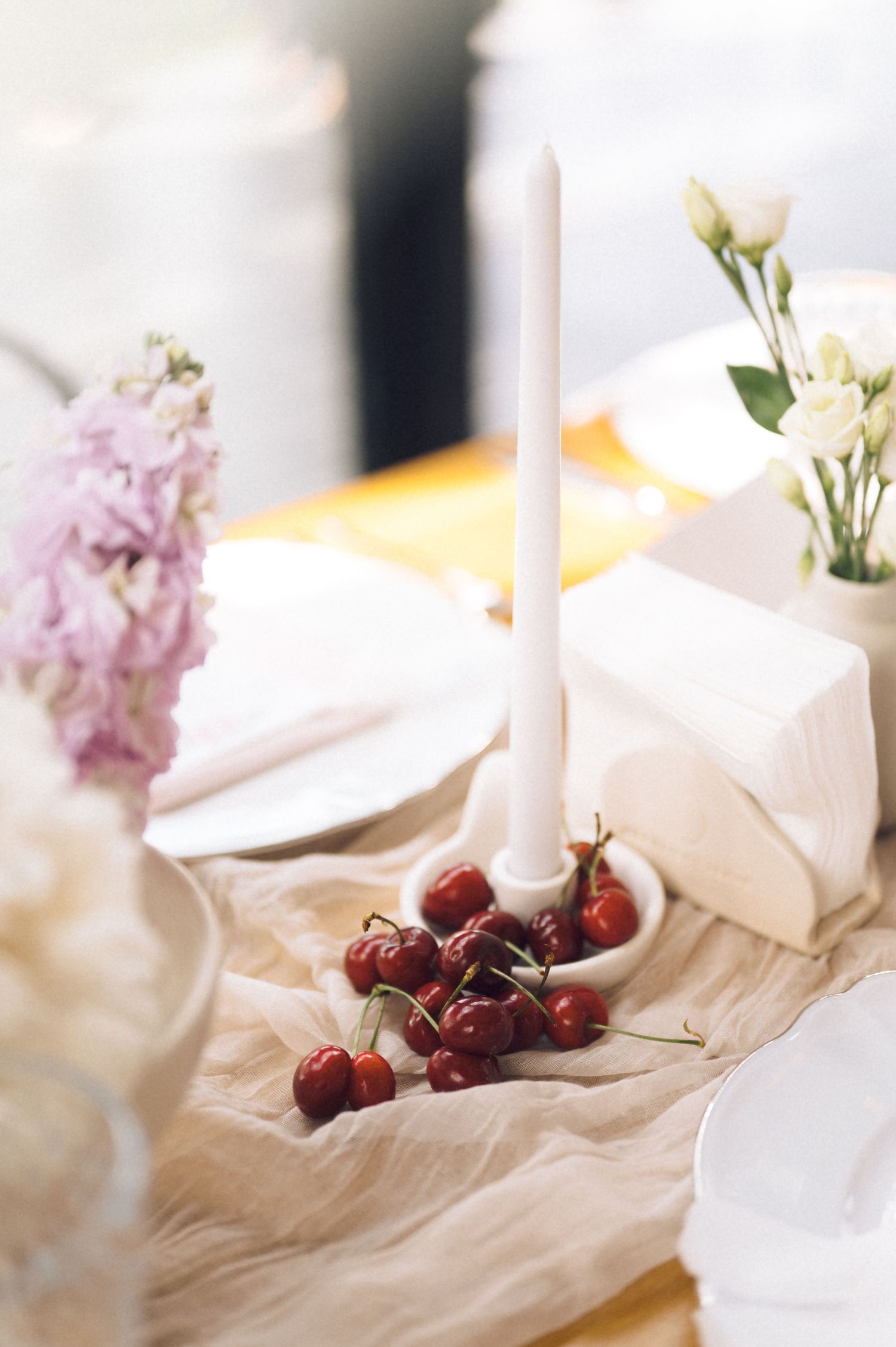 Elegant table setting with cherries, white candle, fresh flowers, and linen runner for a romantic dining experience.