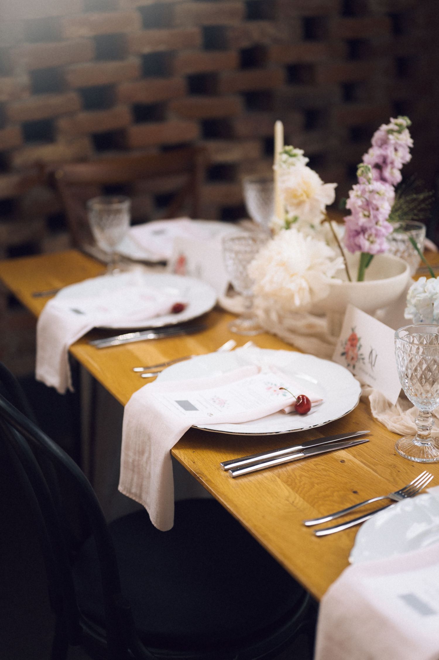 Elegant wedding table setting with white plates, linen napkins, crystal glasses, and fresh floral centerpieces on a wooden table.