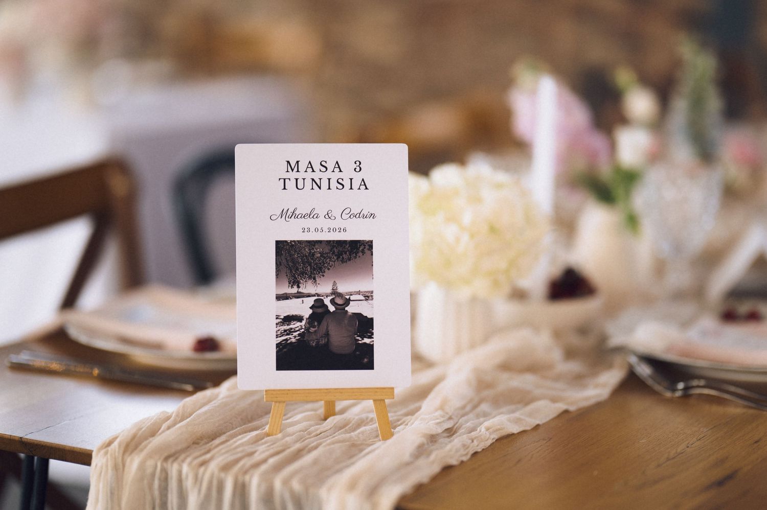 Elegant wedding table setting with a Tunisia table number card on a small easel, featuring floral arrangements and lace runner.