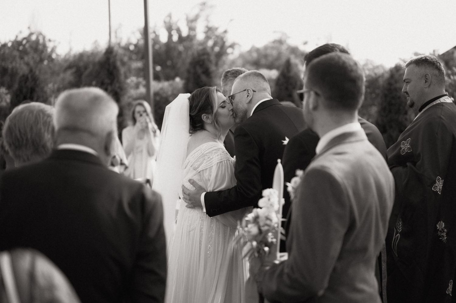 Black and white photo of a bride and groom sharing their first kiss at an outdoor wedding ceremony.