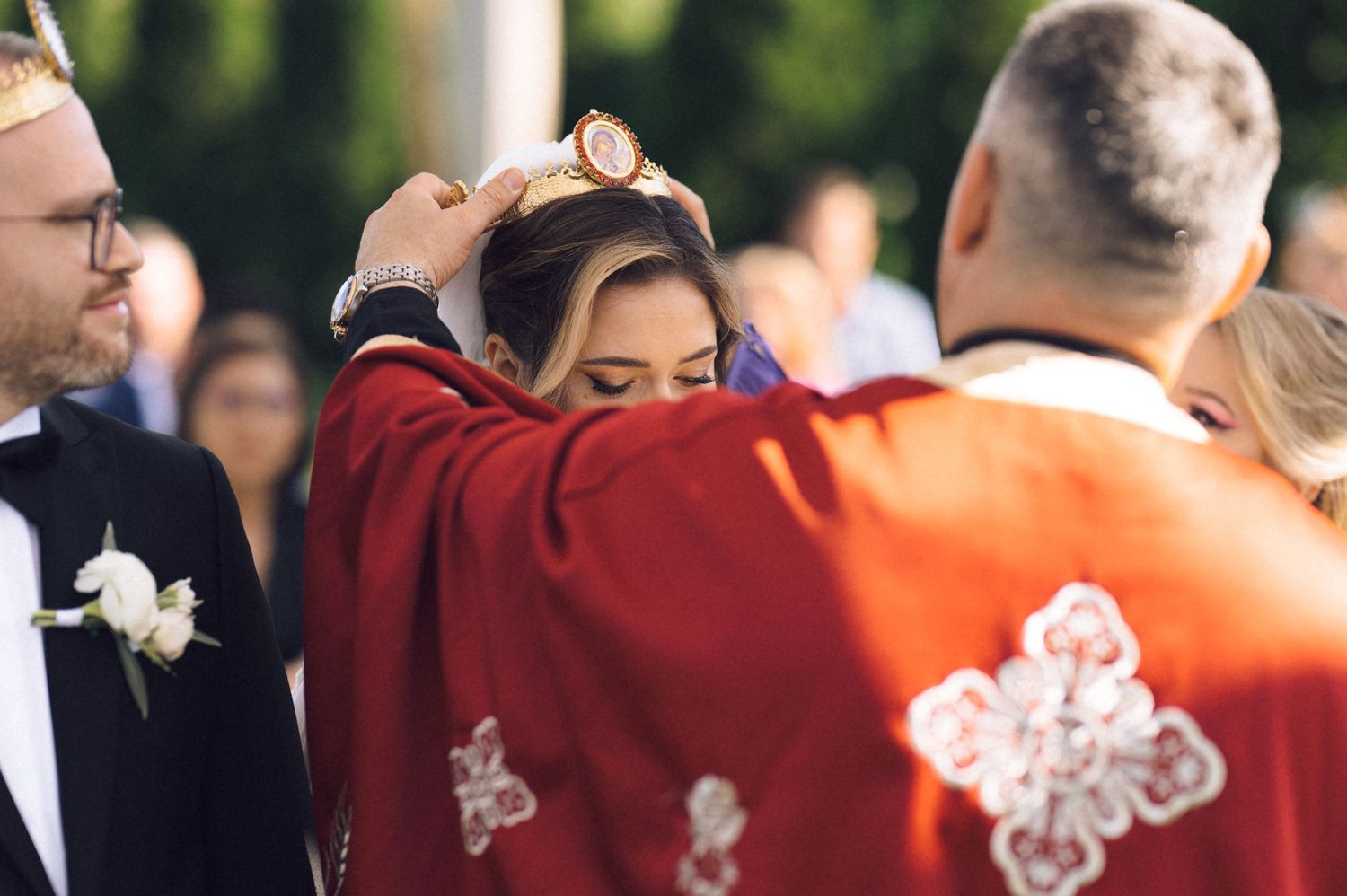 Orthodox priest placing a crown on a bride during a traditional wedding ceremony outdoors.