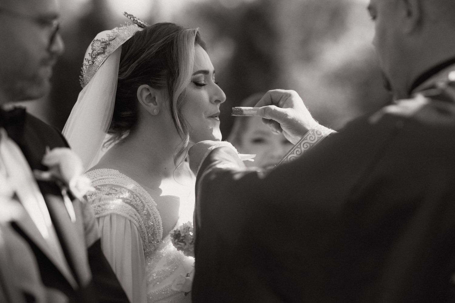 Black and white wedding photo of bride receiving communion during ceremony, wearing veil and gown.