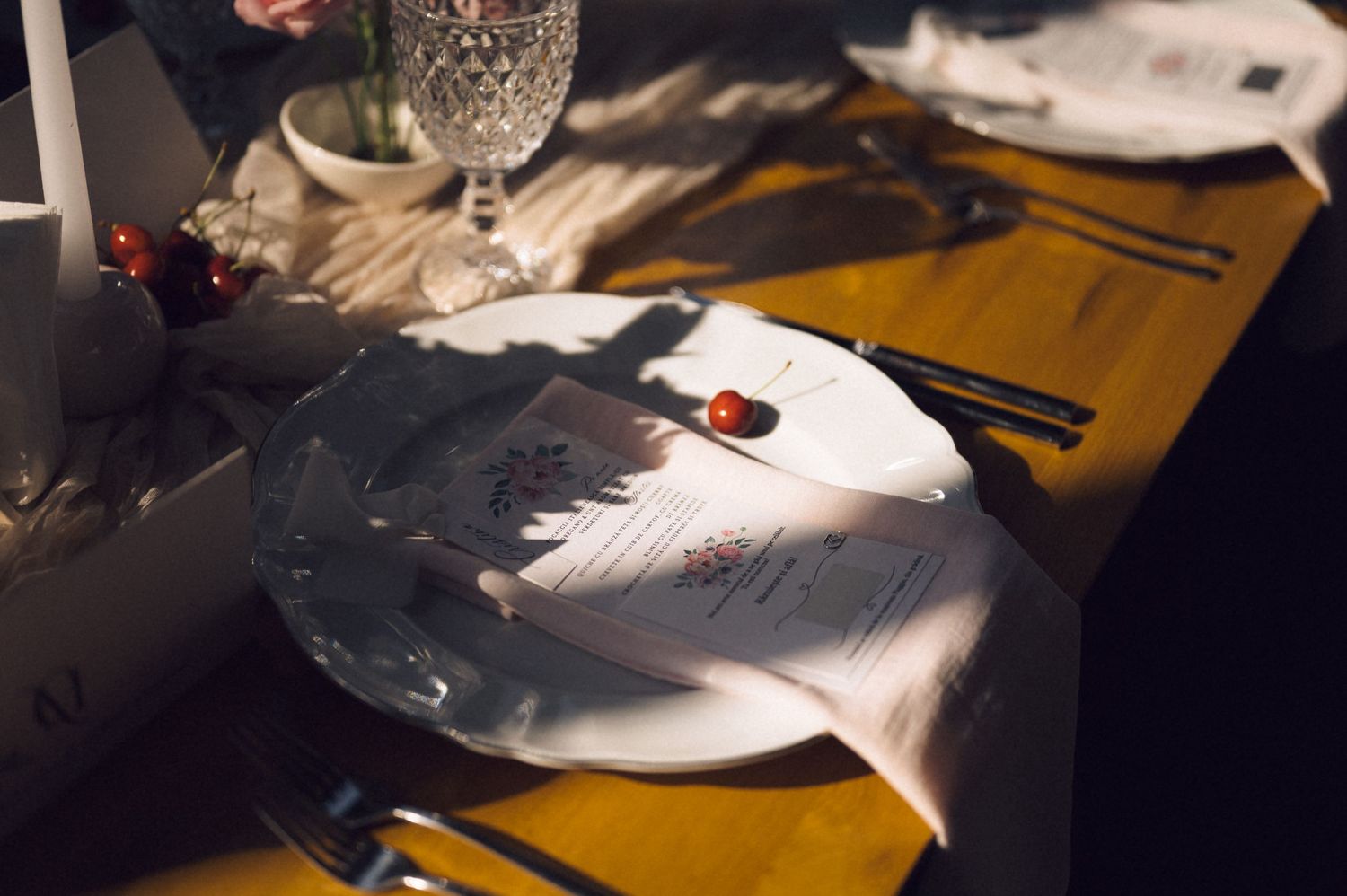 Elegant table setting with white plate, menu card, crystal glass, and cutlery on wooden table.
