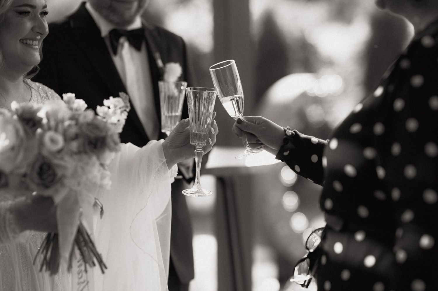Black and white photo of wedding guests clinking champagne glasses in a celebratory toast at a wedding reception.
