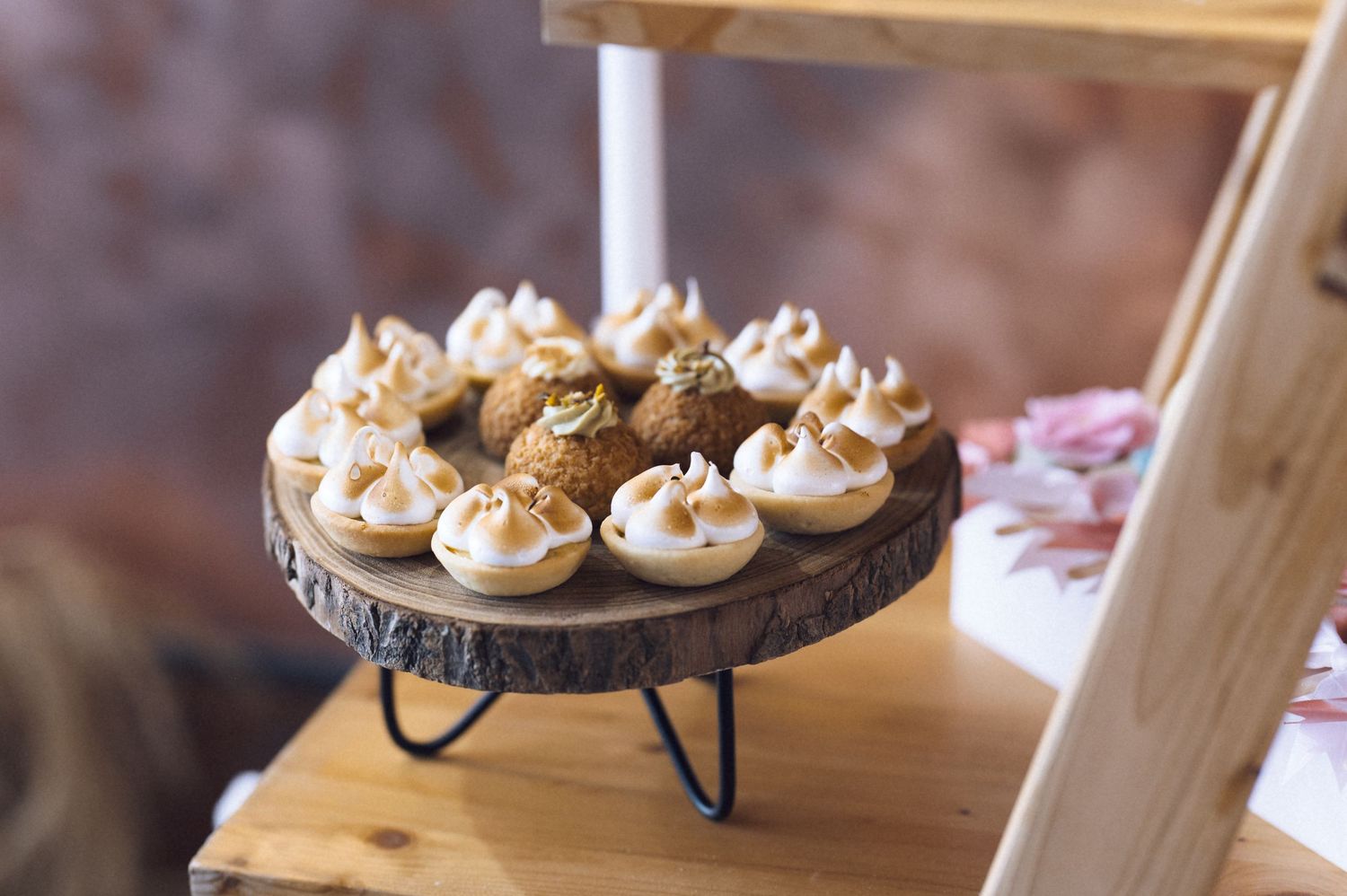 Rustic wooden cake stand displaying elegant mini meringue tarts with golden-brown tops at a dessert table.