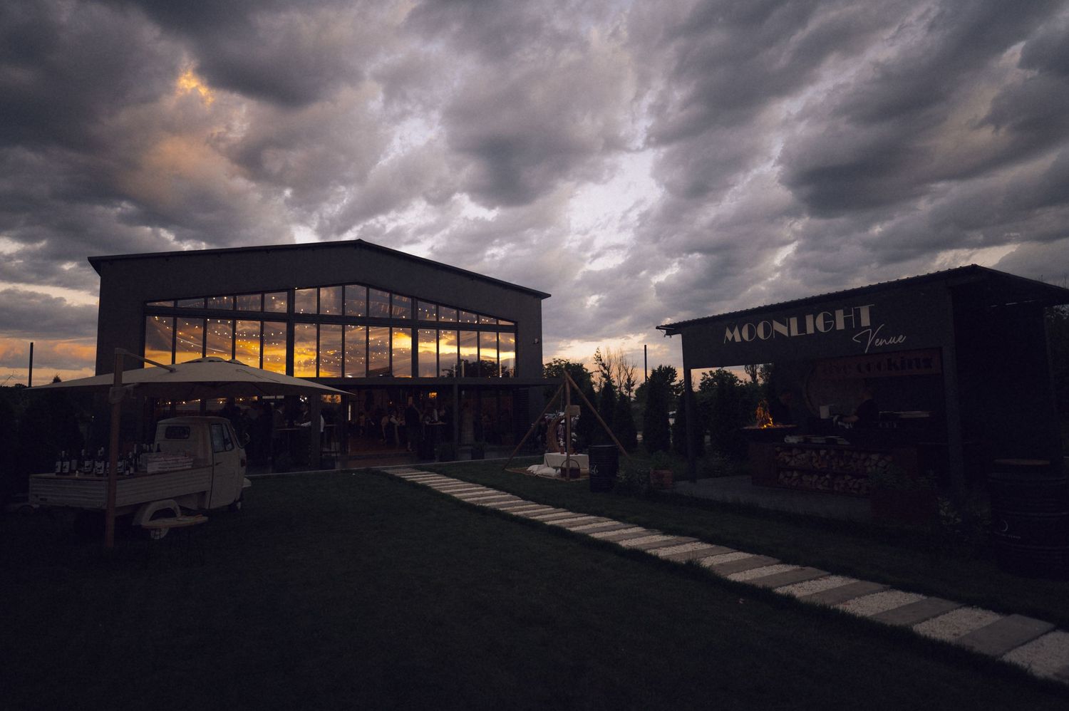 Moonridge venue exterior at dusk with dramatic stormy clouds and warm glowing lights illuminating the building.