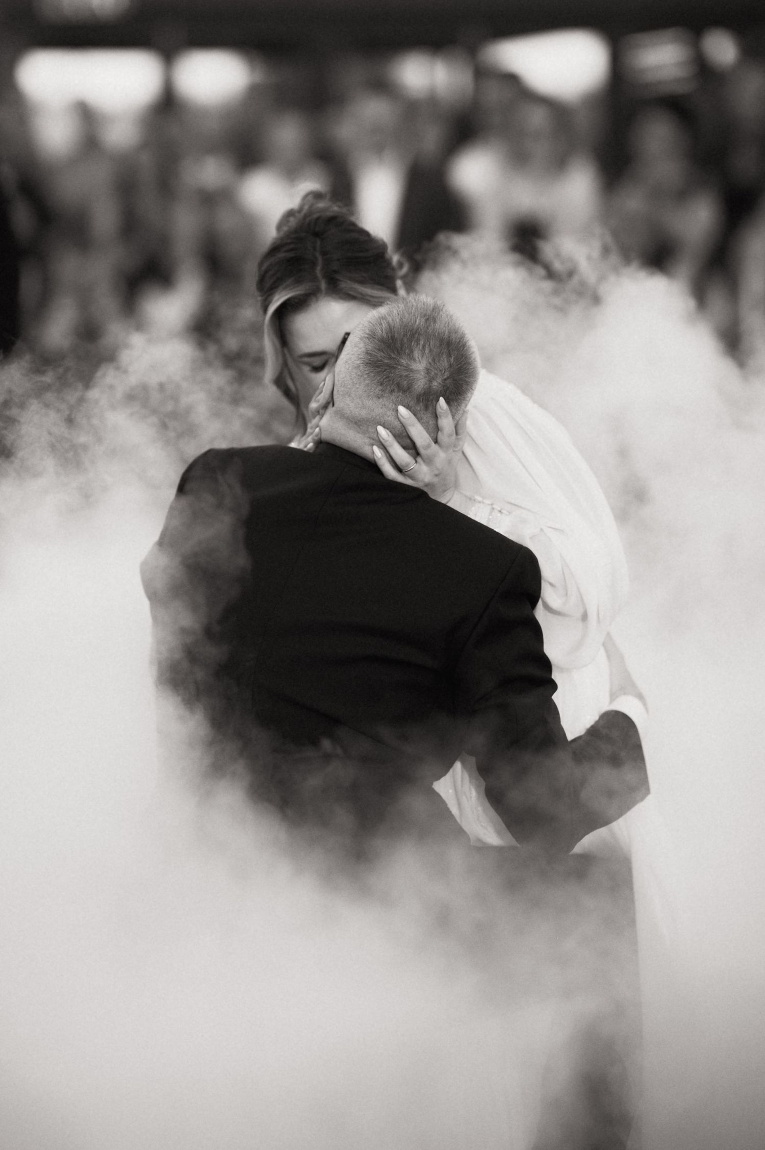 Black and white photo of bride and groom sharing first dance surrounded by dramatic fog at wedding reception.