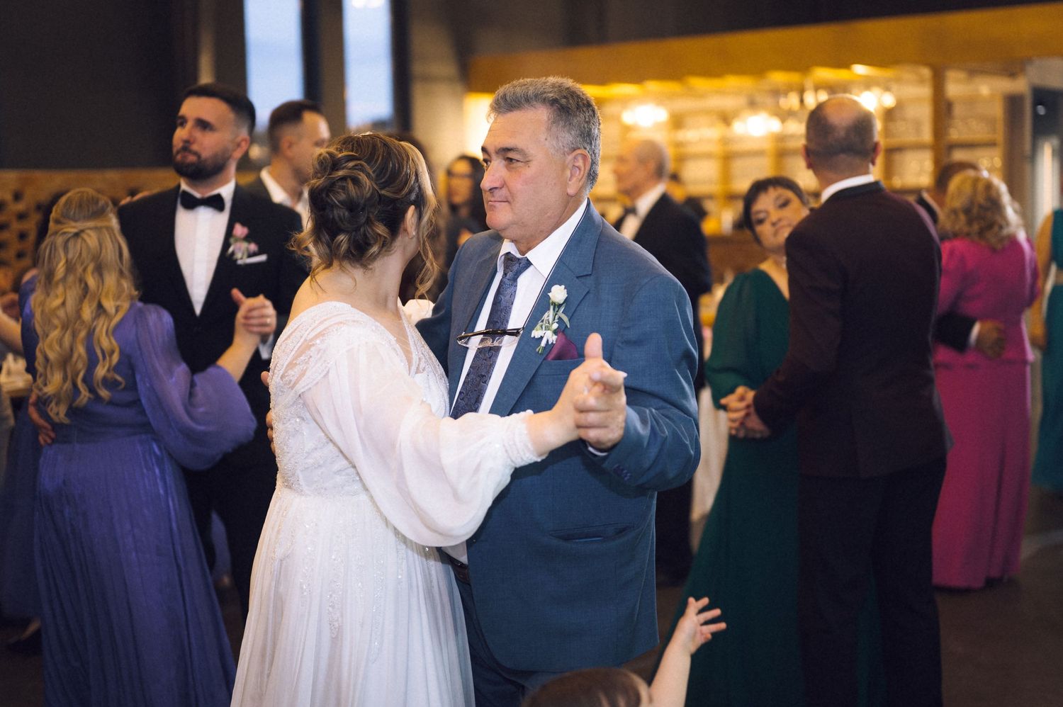 Bride and father sharing a tender first dance at a wedding reception with guests dancing in the background.