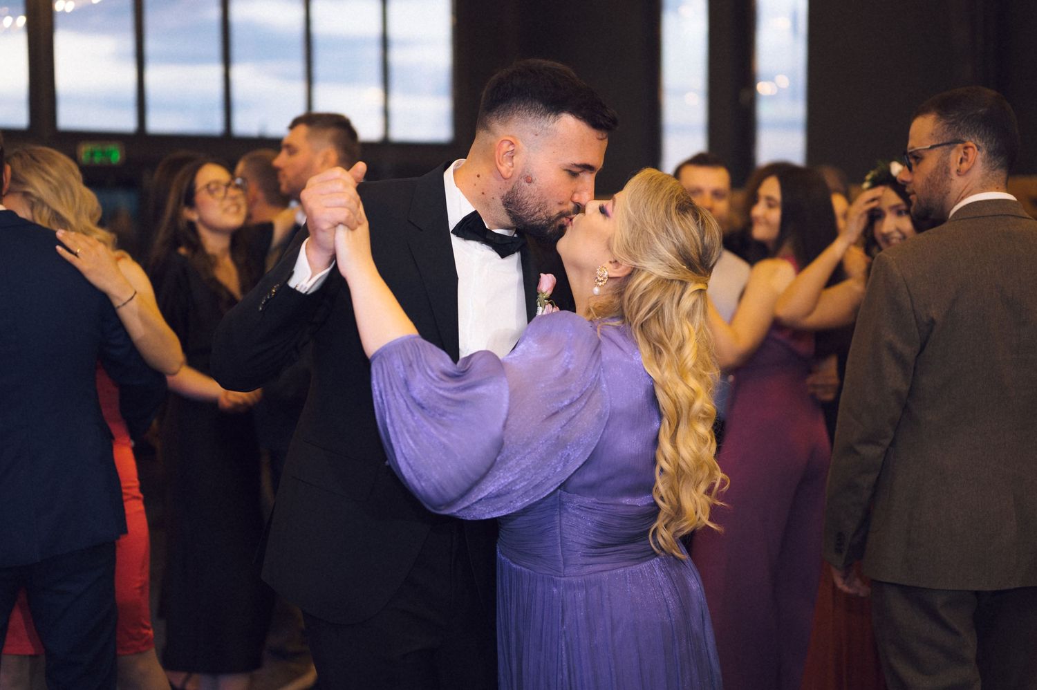 Couple sharing a romantic dance at a formal event, man in tuxedo and woman in purple gown.