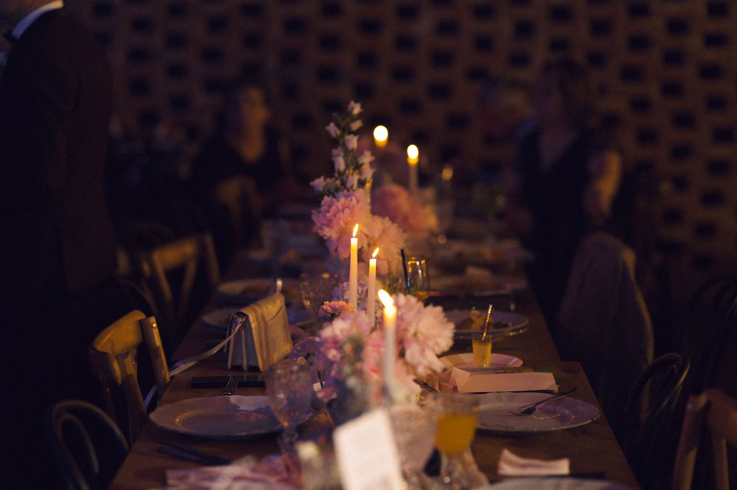 Elegant candlelit dinner table with pink floral centerpieces and golden place settings at a romantic evening event.