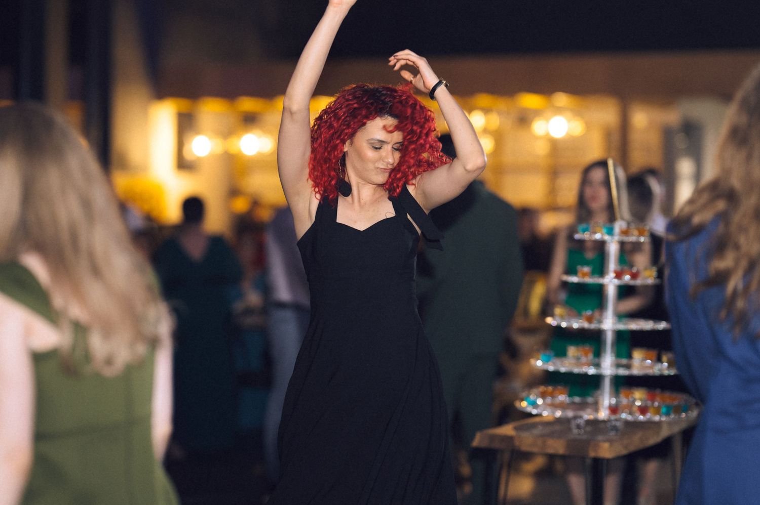Woman with red curly hair dancing in black dress at an elegant evening party event.