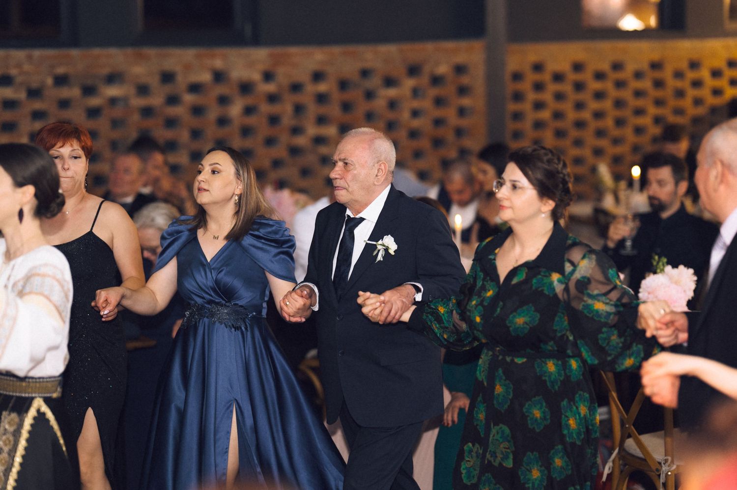 Elegantly dressed guests dancing together at a formal wedding reception in a warmly lit venue.