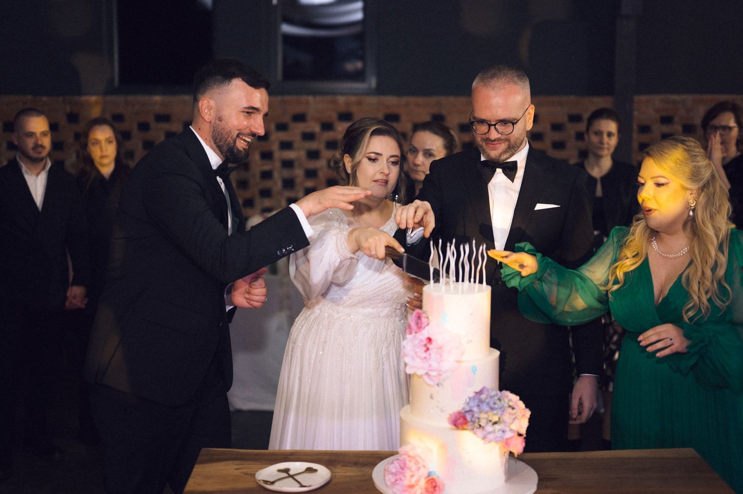 Elegant wedding cake cutting ceremony with bride, groom, and guests in formal attire at a reception venue.