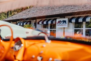 Orange vintage convertible car parked in front of a boutique shop with black and white striped awnings.