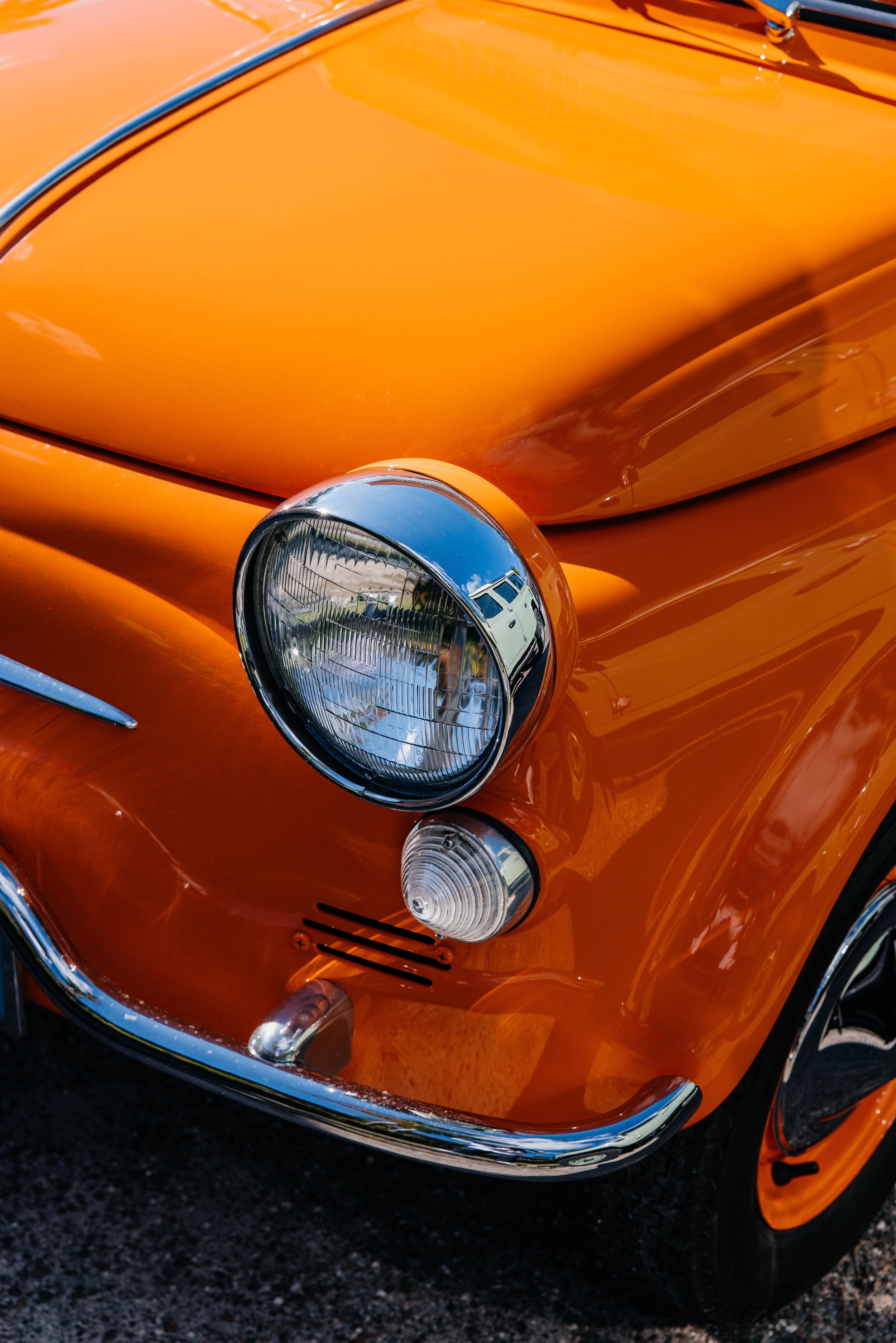 Close-up of a vintage orange Fiat 500 classic car showcasing its round chrome headlight and shiny bumper.