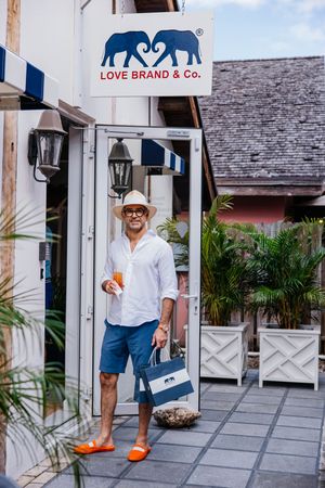 Man in white shirt, blue shorts, and orange sandals holding a bag outside Love Brand & Co. store.