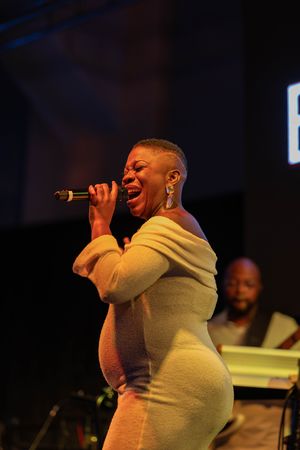 Pregnant female vocalist performing passionately on stage under warm lights at a live music event.