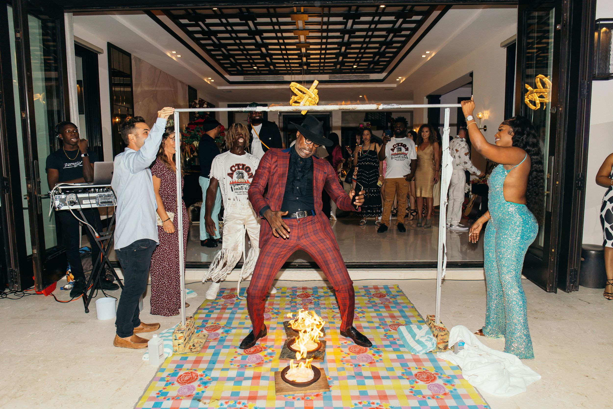 A performer in red sequin outfit dances energetically at a vibrant party with musicians and guests celebrating around him.
