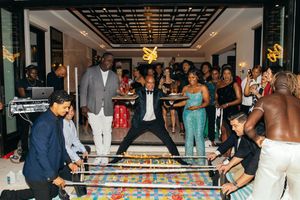 Guests celebrate at an elegant party with a large decorated cake table, DJ, and festive balloon decorations.