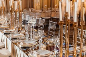 Elegant wedding reception table with gold candelabras, crystal glassware, and chiavari chairs in a luxurious ballroom.