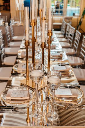 Luxurious wedding reception table with gold candelabras, crystal glassware, and mirrored surface.