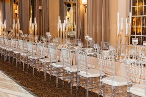 Elegant banquet hall with long tables, clear chiavari chairs, and tall gold candelabras.