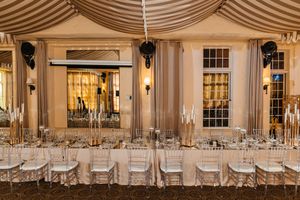 Elegant banquet hall with long tables, crystal chairs, gold candelabras under a striped tent.