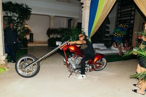 Person riding a red custom chopper motorcycle inside a luxurious indoor venue with tropical decor.