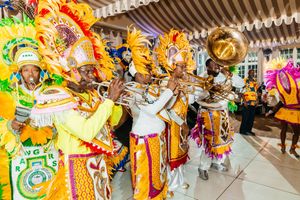Colorful Junkanoo festival performers in vibrant costumes playing brass instruments during a lively Caribbean street parade celebration.