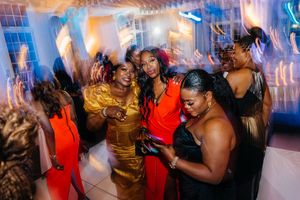 Women dancing and celebrating at a lively party event, wearing colorful dresses under dynamic lighting.