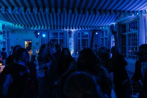Crowd of people dancing under blue lights and striped awning at an indoor party event.