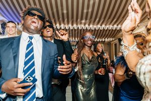 Guests in masks and formal attire dance joyfully at an elegant indoor party celebration.