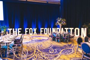 Elegant Fox Foundation gala event setup with marquee letters, floral centerpieces, and ornate blue patterned carpet.