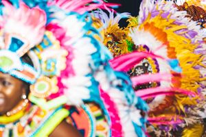 Vibrant carnival performers in colorful feathered costumes with pink, blue, and yellow headdresses at a festive parade.