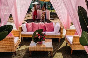 Outdoor lounge area with wicker furniture, pink cushions, floral centerpiece, and pink draped curtains at an elegant event.