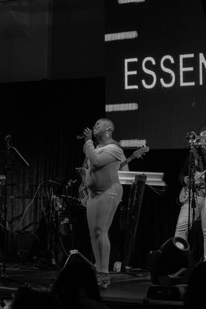 Black and white photo of a pregnant singer performing on stage at Essence Festival, holding a microphone.