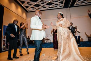 Bride in gold gown and groom in white tuxedo share joyful first dance at elegant wedding reception.