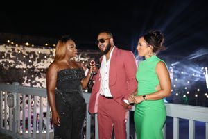 Three elegantly dressed people conversing at an outdoor evening event, with bright lights illuminating the night sky.